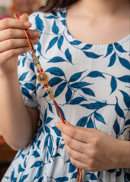 A woman in a blue and white patterned dress holds a colorful traditional Indian Rakhi thread.