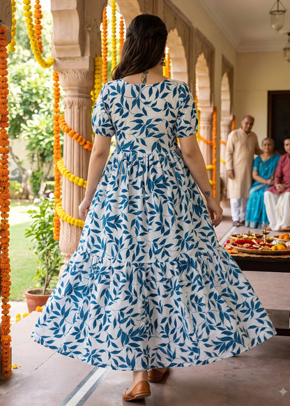A woman wearing a blue and white patterned tiered maxi dress walks in a traditional courtyard decorated with yellow marigold garlands.