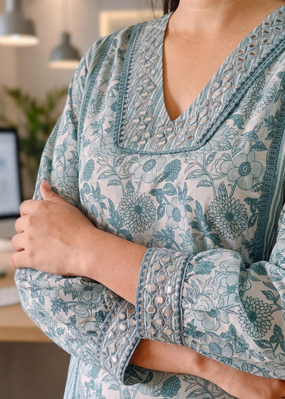 A close-up of a woman wearing a long-sleeve V-neck kurta with a blue and white floral block print and mirror embroidered details on the neckline and cuffs.