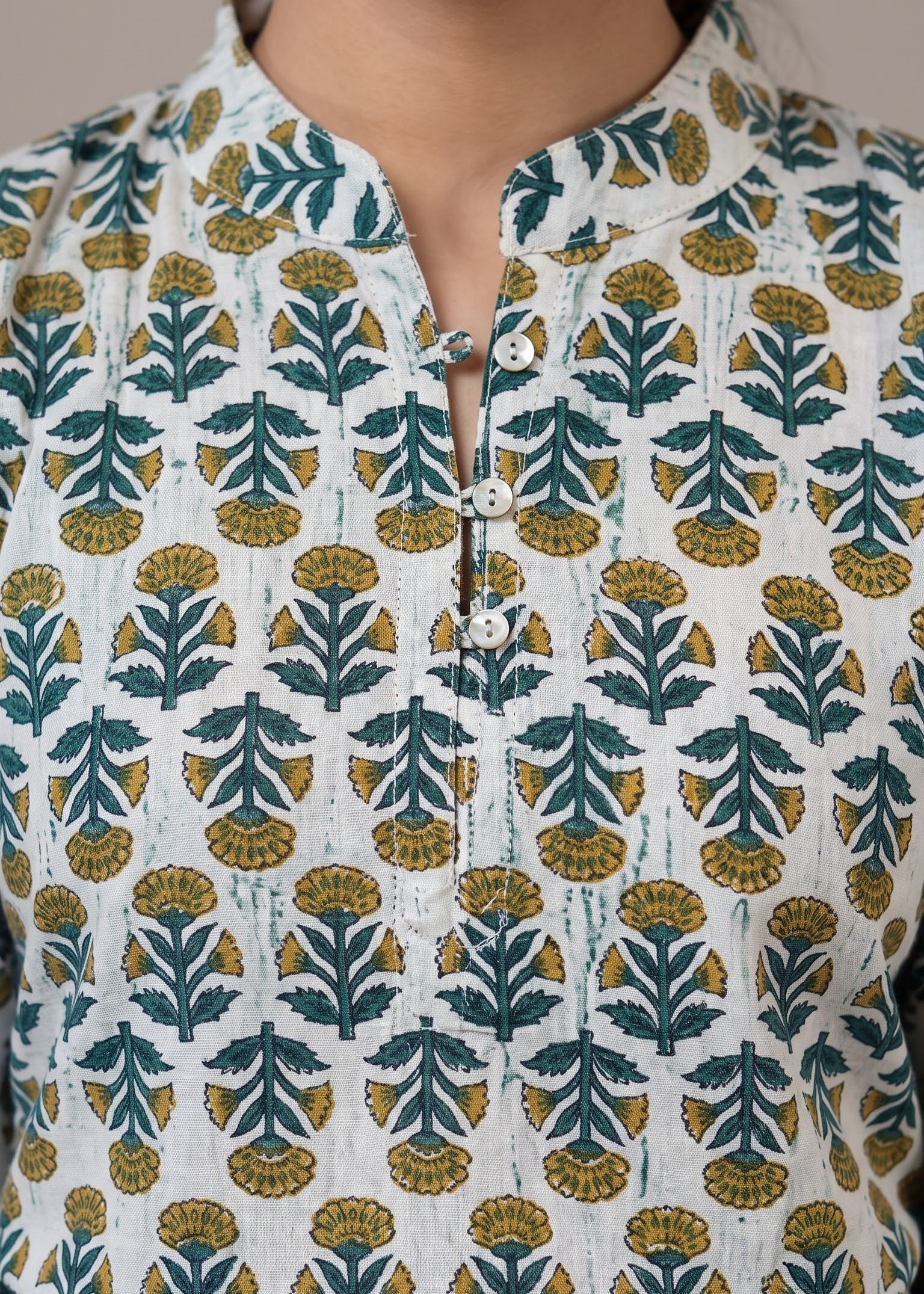 A close-up of a person wearing a white batik button-front top with a repeating teal and mustard yellow leaf block-print pattern, paired with blue jeans.