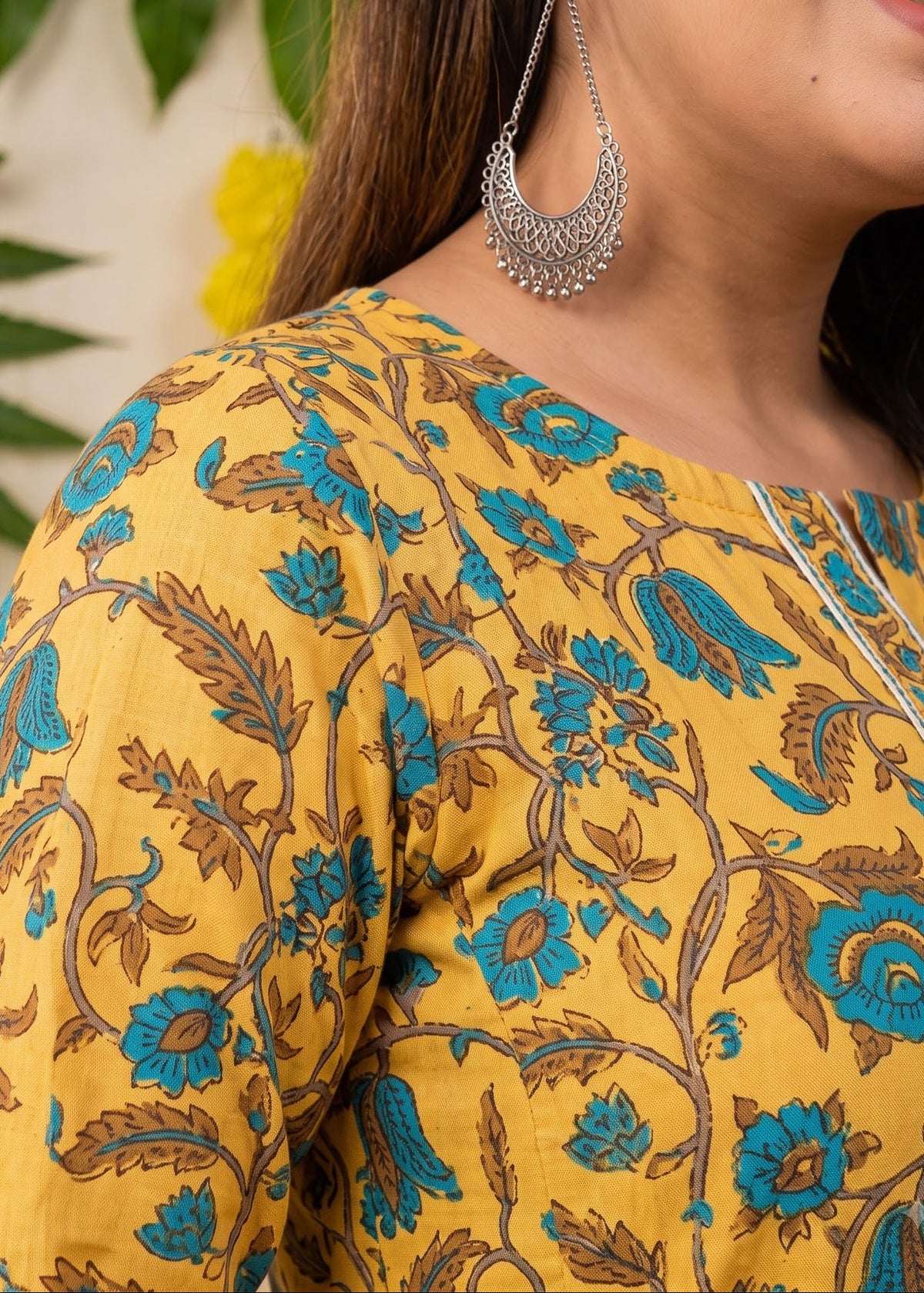 A close-up of a woman wearing a mustard yellow printed maternity kurta dress with blue and brown floral patterns.
