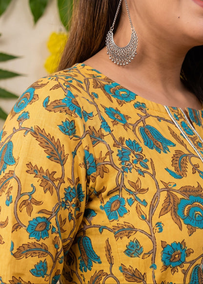 A close-up of a woman wearing a mustard yellow printed maternity kurta dress with blue and brown floral patterns.