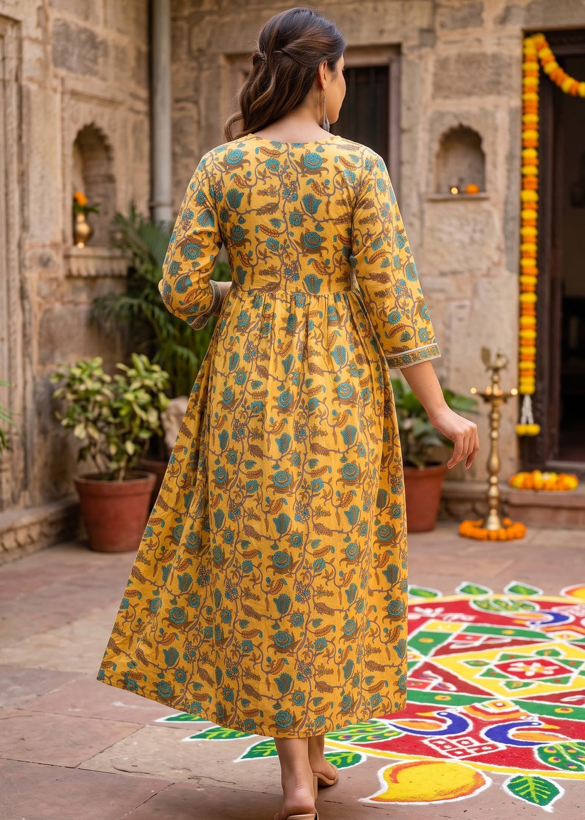 A woman viewed from behind wearing a yellow and teal floral print maternity kurta dress in an outdoor courtyard.