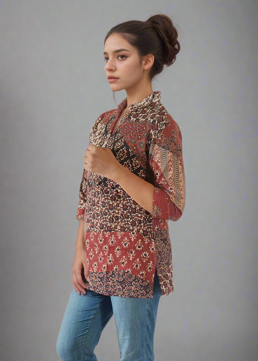 Woman wearing a patterned tunic shirt top and jeans on a plain background