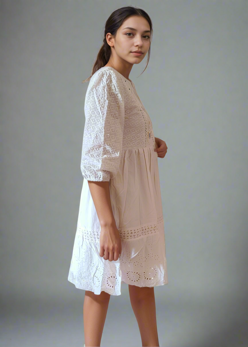 Woman wearing a white dress with white lace details on a plain background