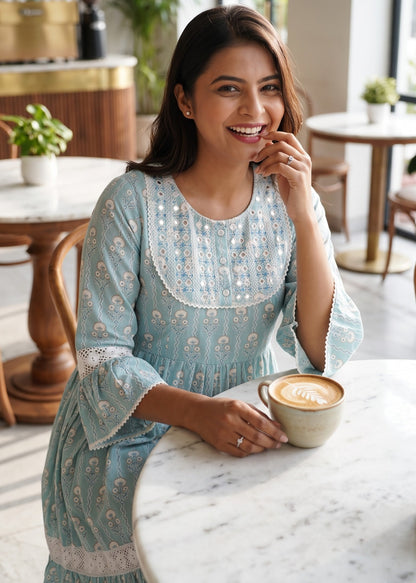 A woman wearing a light blue mirror embroidered short dress at a marble table in a cafe, holding a cup of coffee.