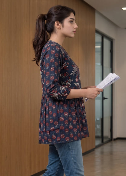 A woman in a side profile wearing a navy blue floral printed tunic short kurti top and blue jeans, holding a stack of papers in an indoor office hallway.