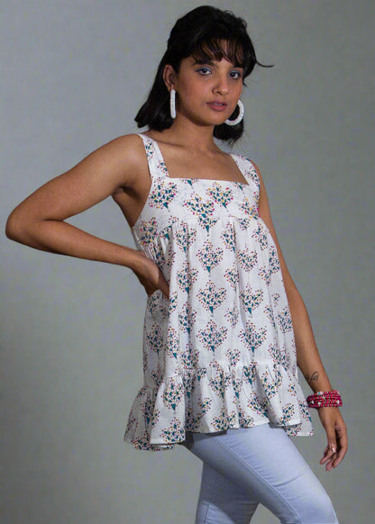 Woman wearing a white floral blouse top and light blue leggings against a black background