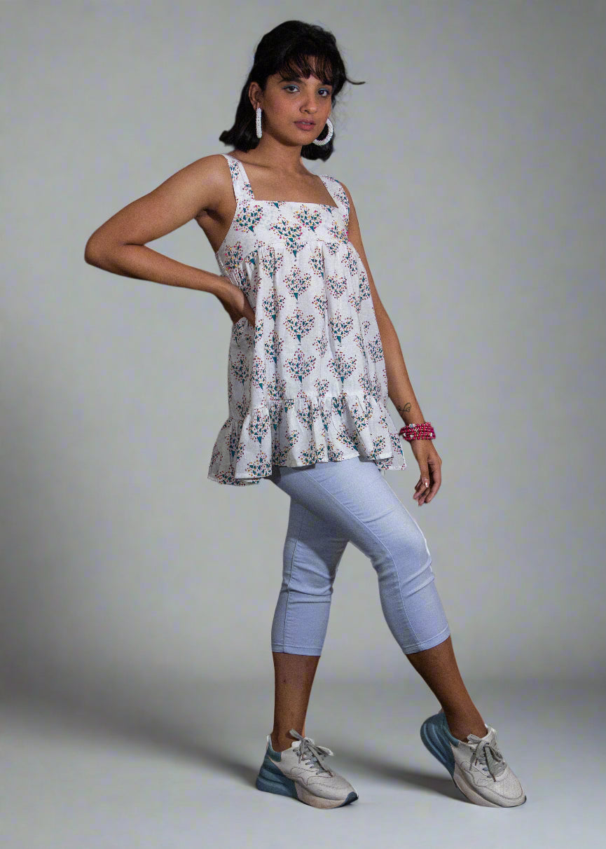 Woman wearing a white floral blouse top and light blue leggings against a black background